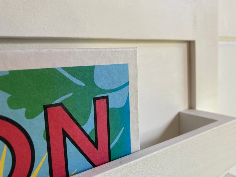 May include: Close-up of a colorful print with the letter "N" in red with a black outline. The print is partially inserted into a white shelf.