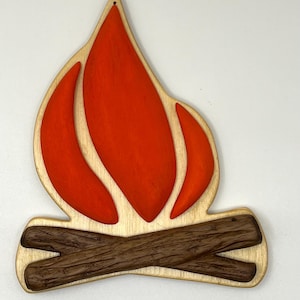 May include: A wooden cutout of a campfire with orange flames and brown logs. The cutout is made of wood and has a rustic look.