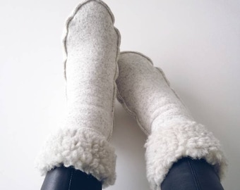 Könnte beinhalten: Ein Paar weiße, flauschige Hausschuhe mit einem gewellten Rand. Die Socken werden von jemandem getragen, der schwarze Leggings trägt.