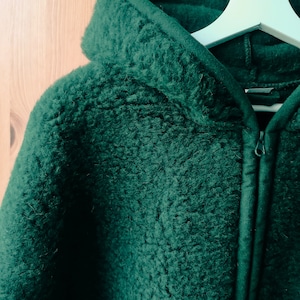 May include: A dark green hooded jacket with a zip closure. The jacket is made of a soft, fuzzy material.