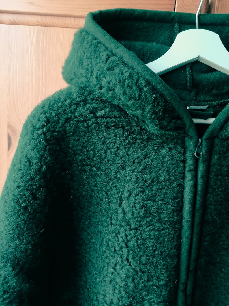 May include: A dark green hooded jacket with a zip closure. The jacket is made of a soft, fuzzy material.