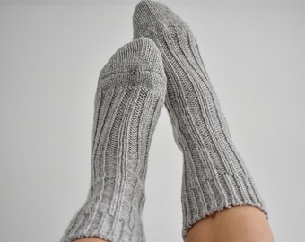 May include: A pair of grey ribbed knit socks. The socks are pulled up, with the feet and lower legs visible against a white background. The socks have a textured, vertical rib pattern.