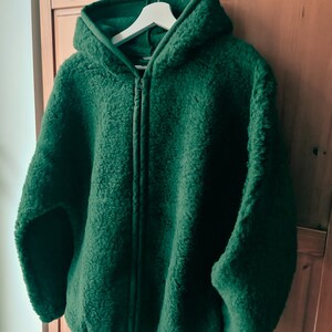 May include: A dark green hooded fleece jacket with a zip closure. The jacket is hanging on a white hanger.