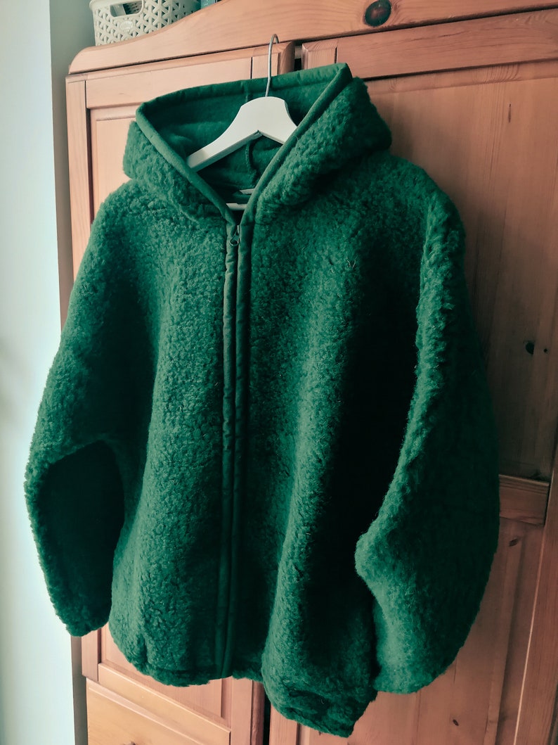 May include: A dark green hooded fleece jacket with a zip closure. The jacket is hanging on a white hanger.