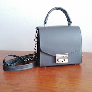 May include: A small gray leather handbag with a top handle and a chain strap. The bag has a silver clasp and a flap closure.