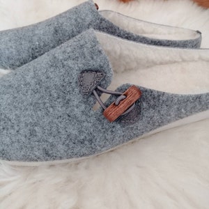 May include: A pair of grey felt slippers with a wooden button detail. The slippers have a white fleece lining.
