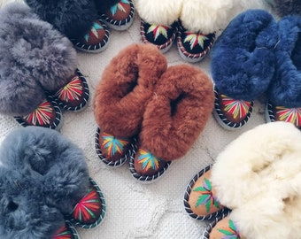 May include: A selection of fluffy slippers with colourful embroidery. The slippers are made from sheepskin and come in a range of colours, including brown, white, grey, and blue.