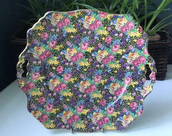 May include: A black and gold serving tray with a floral pattern. The tray has two handles and a scalloped edge.
