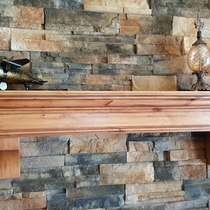May include: A wooden mantel shelf with a decorative metal airplane and a glass lamp on top. The shelf is mounted on a stone wall.