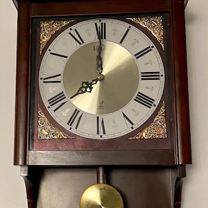 Vintage wall clock, Jaz Quartz, battery-powered movement, cherry wood body, pendulum, Roman numerals, black iron hands, year 1985