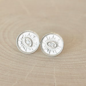 May include: A pair of silver earrings with a circular design featuring a stylized eye with a small diamond in the center.