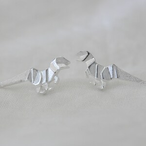 May include: A pair of silver origami dinosaur earrings. The dinosaurs are facing each other.