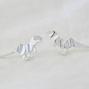 May include: A pair of silver origami dinosaur earrings. The dinosaurs are facing opposite directions.