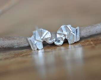 May include: A pair of silver elephant stud earrings. The elephants are facing each other and have a geometric design.