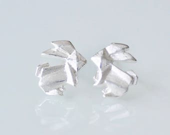 May include: A pair of silver origami rabbit stud earrings. The earrings are made of a textured, geometric design.