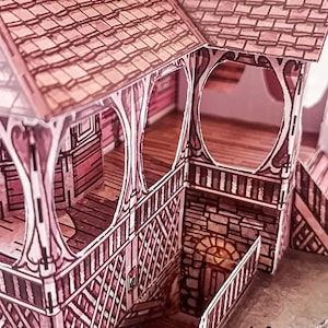 May include: A paper model of a pink and brown house with a detailed porch and a stone basement. The house has a gabled roof with a shingled pattern and a decorative railing around the porch.