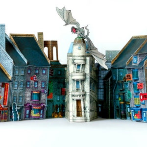 May include: A detailed paper model of a street lined with colorful buildings, featuring various architectural styles. A dragon figure is perched atop one building. The buildings have signs and window details, creating a miniature cityscape.