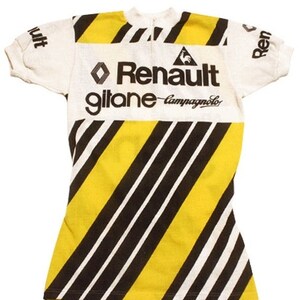 May include: A white cycling jersey with black and yellow diagonal stripes. The jersey has the logos "Renault", "gitane", and "Campagnolo" printed on the front.