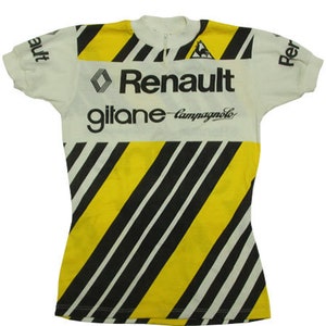 May include: White and yellow cycling jersey with black diagonal stripes and the Renault, Gitane, and Campagnolo logos. The jersey has short sleeves and a partial zipper at the collar.