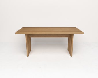 Op de afbeelding: Een eenvoudige, rechthoekige houten tafel met een lichtbruine afwerking. De tafel heeft een vlak blad en twee poten aan elke kant.