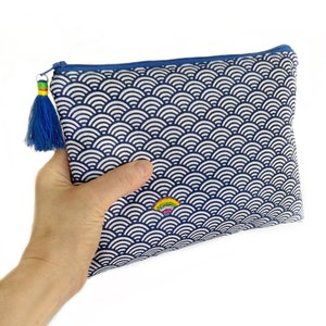 Peut inclure: Une pochette zippée bleue et blanche avec un motif brodé arc-en-ciel. La pochette est dotée d'un pompon bleu attaché à la fermeture éclair.