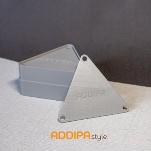 May include: Three grey triangular objects with rounded corners and three holes. One triangle is separate, showing the word "ADDIPA" embossed on the surface. The logo "ADDIPAstyle" is at the bottom.