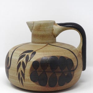 May include: A ceramic pitcher with a rounded body and a spout. The pitcher is tan with black abstract leaf and teardrop designs. It has a black handle and is suitable for serving beverages.
