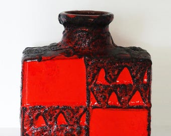 May include: A rectangular ceramic vase featuring a vibrant red glaze contrasted with dark brown, textured lava-like drip patterns. The vase has a short, cylindrical neck and a flat top edge, with a geometric design of solid red squares and textured brown zig-zag motifs.