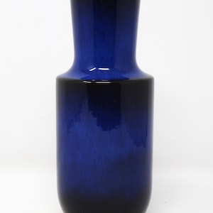 May include: A tall, elegant vase with a gradient of blue hues, transitioning from a deep indigo at the base to a vibrant cobalt at the top. The ceramic vase has a smooth, glossy finish and a slightly flared opening.