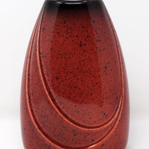 May include: A ceramic vase with a speckled, reddish-brown finish. The vase has a curved, elongated shape with a dark brown top. Two curved lines are etched into the surface, adding a decorative element. The vase is approximately 8 inches tall.