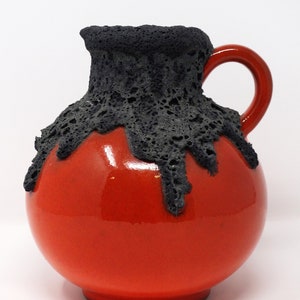 May include: A red ceramic pitcher with a black lava glaze. The glaze has a textured, dripping effect.