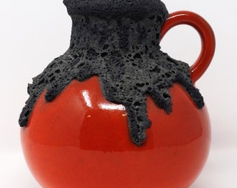 Pode incluir: Um jarro de cerâmica vermelho com um esmalte de lava preto. O esmalte tem um efeito texturizado e de gotejamento.