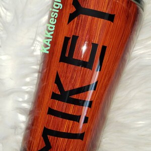 May include: A brown and black stainless steel tumbler with a wood grain design and the name "MIKEY" printed in black letters.