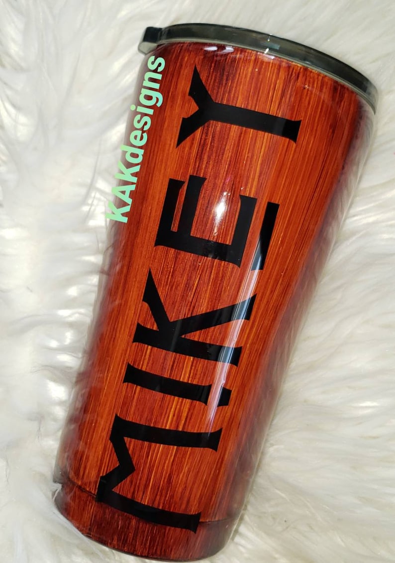 May include: A brown and black stainless steel tumbler with a wood grain design and the name "MIKEY" printed in black letters.