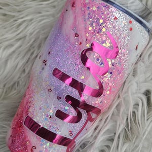 Puede incluir: Un vaso cubierto de purpurina con un dise&ntilde;o de m&aacute;rmol rosa y blanco. El vaso presenta el nombre "Skylar" en una fuente rosa brillante y brillante. El dise&ntilde;o incluye confeti en forma de coraz&oacute;n.