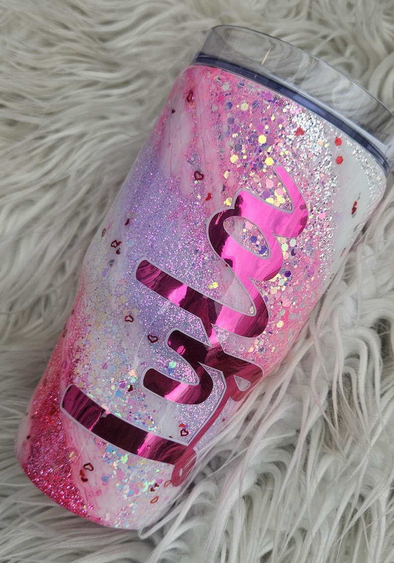 Puede incluir: Un vaso cubierto de purpurina con un dise&ntilde;o de m&aacute;rmol rosa y blanco. El vaso presenta el nombre "Skylar" en una fuente rosa brillante y brillante. El dise&ntilde;o incluye confeti en forma de coraz&oacute;n.