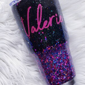 May include: A black and purple glitter tumbler with a clear lid. The tumbler has the name "Valerie" written in pink cursive on the side.