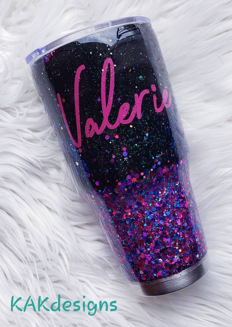 May include: A black and purple glitter tumbler with a clear lid. The tumbler has the name "Valerie" written in pink cursive on the side.