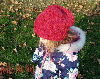 May include: A young person wearing a red crocheted hat with a braided design. The hat is worn over a floral patterned jacket with a white fur trim.