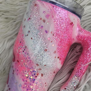 Puede incluir: Un vaso con purpurina y asa, con un dise&ntilde;o rosa, blanco y plateado. El vaso est&aacute; adornado con confeti en forma de coraz&oacute;n. La tapa es transparente con un deslizador blanco. Esta taza aislada est&aacute; dise&ntilde;ada para bebidas fr&iacute;as o calientes.