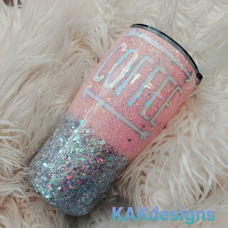 Puede incluir: Un vaso de glitter rosa y plateado con la palabra "COFFEE" escrita en blanco en la parte rosa. El vaso tiene una tapa negra.