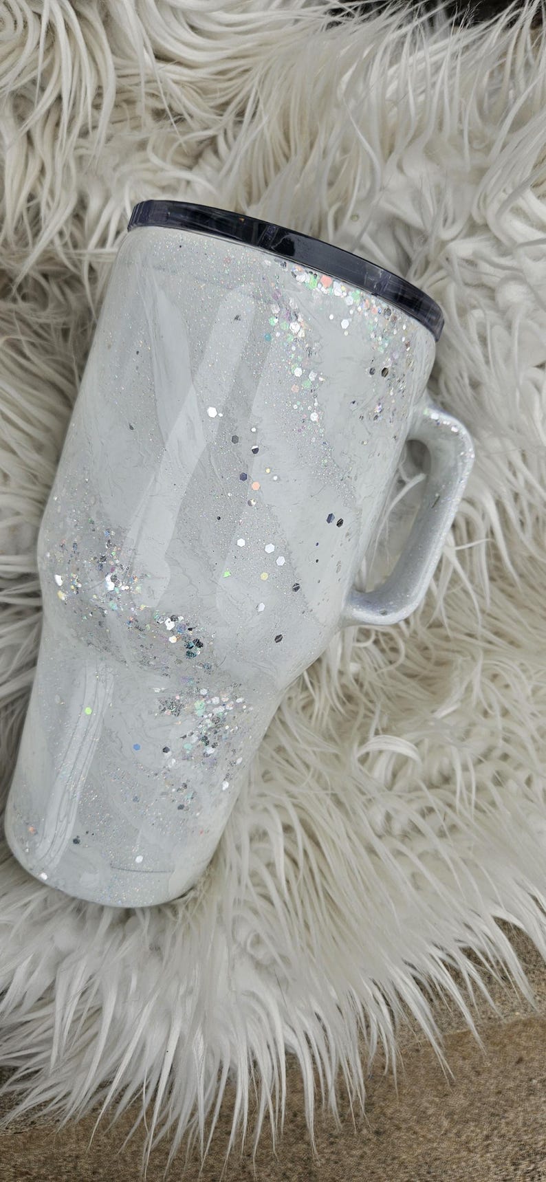 May include: A white travel mug with a black lid and a handle. The mug is covered in silver glitter.
