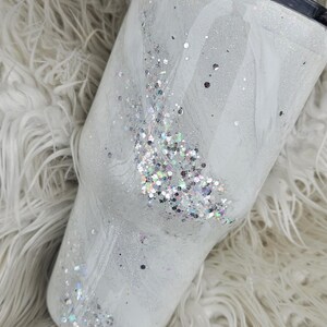 May include: White tumbler with a swirl design and silver glitter. The tumbler has a black lid.