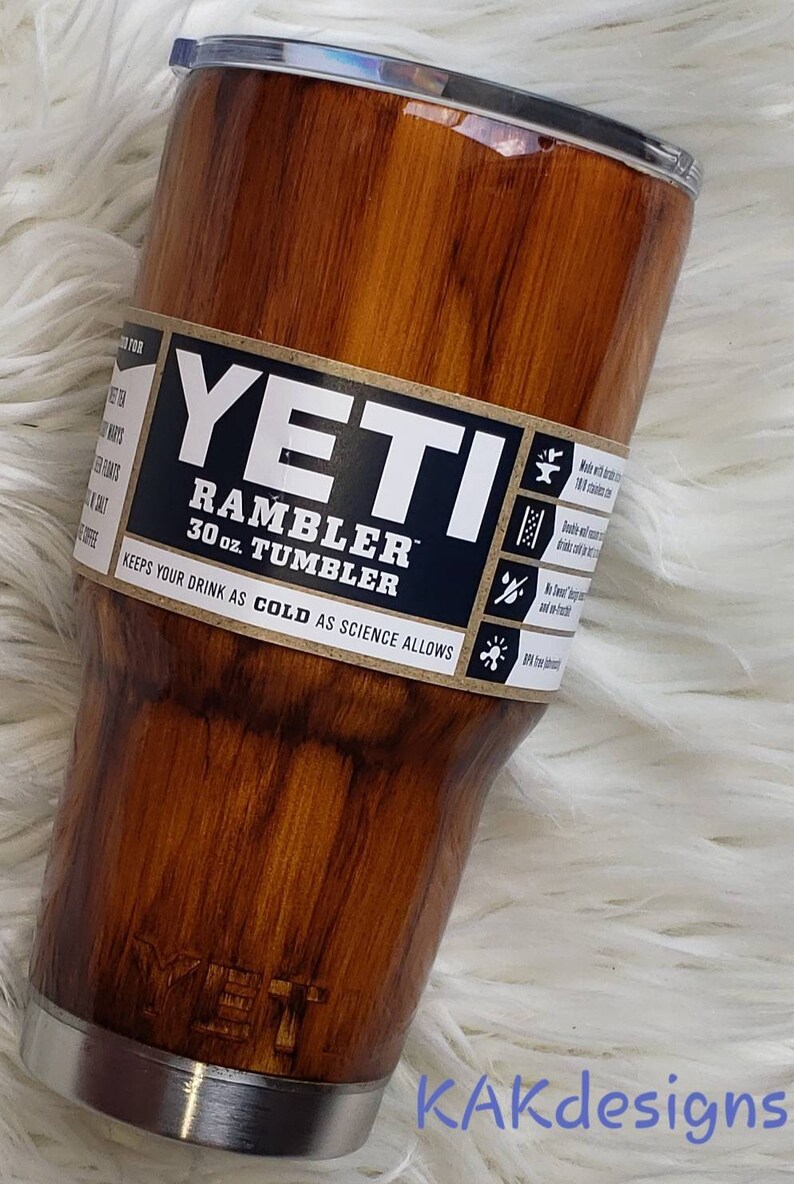 May include: A 30 ounce YETI Rambler Tumbler with a wood grain design. The tumbler is made of stainless steel and has a double-wall vacuum insulation to keep drinks cold. The label on the tumbler says "YETI Rambler 30 oz. Tumbler Keeps your drink as cold as science allows."