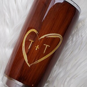 May include: A brown stainless steel tumbler with a wood grain design and a gold heart with the initials "T + T" engraved on it.