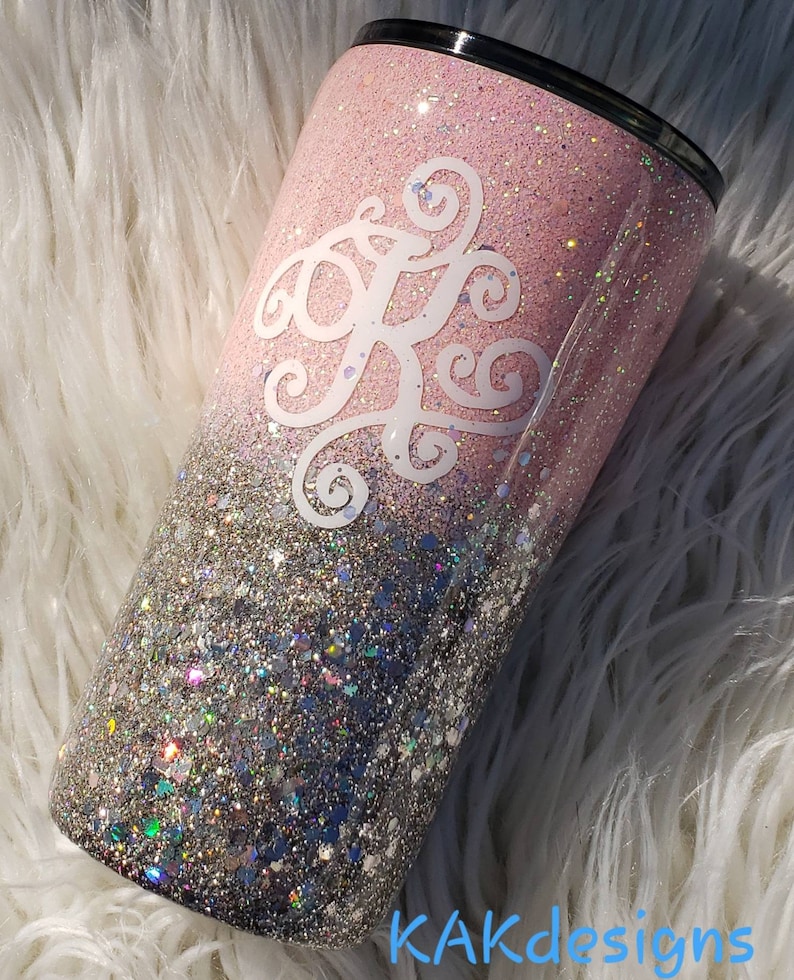 Puede incluir: Un vaso de glitter rosa y plateado con un monograma blanco. El vaso tiene un efecto degradado, con el glitter rosa que se funde en el glitter plateado.