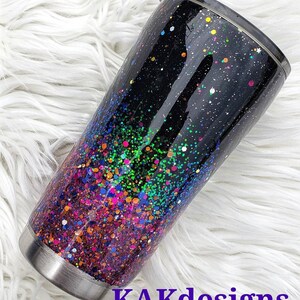 May include: A black stainless steel tumbler with a colourful glitter ombre design. The glitter starts with a dark purple at the bottom and fades to a light green at the top. The tumbler has a black lid with a clear plastic lid.