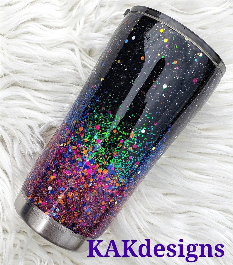 May include: A black stainless steel tumbler with a colourful glitter ombre design. The glitter starts with a dark purple at the bottom and fades to a light green at the top. The tumbler has a black lid with a clear plastic lid.