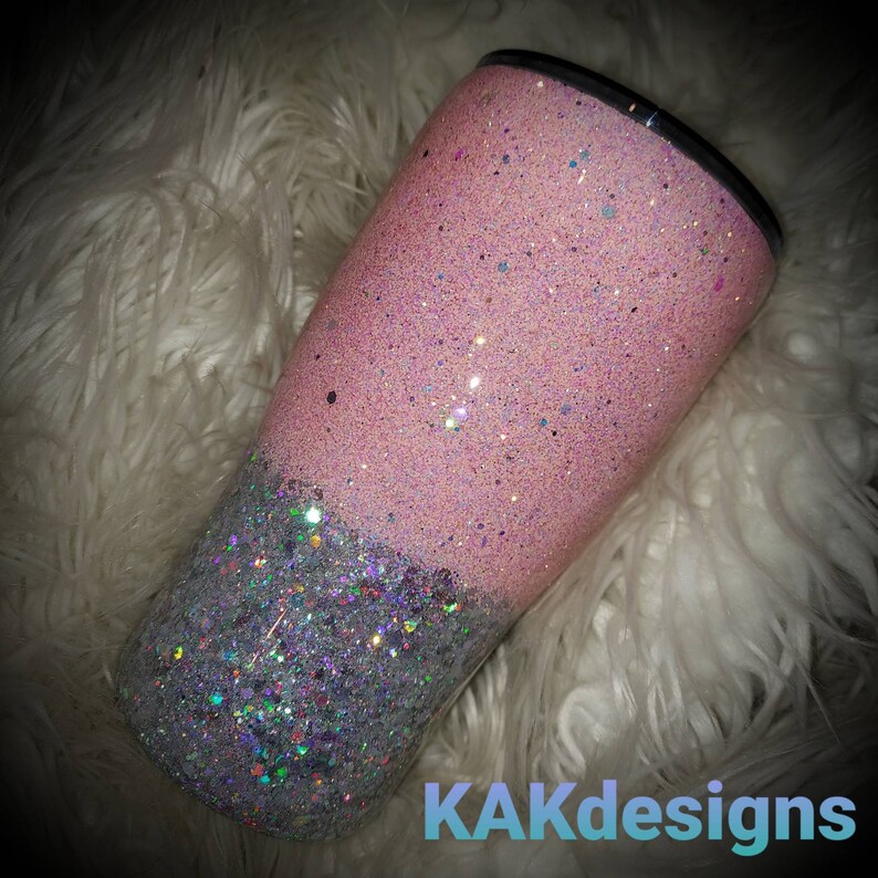 Puede incluir: Un vaso de glitter rosa y plateado con un dise&ntilde;o de dos tonos. La mitad superior es de glitter rosa y la mitad inferior es de glitter plateado. El vaso est&aacute; sobre una superficie blanca y esponjosa. KAKDesigns est&aacute; impreso en la esquina inferior derecha de la imagen.