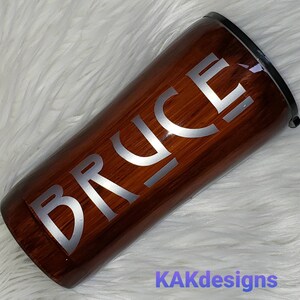 May include: A brown and silver personalized tumbler with the name "BRUCE" printed on it. The tumbler has a wood grain design.